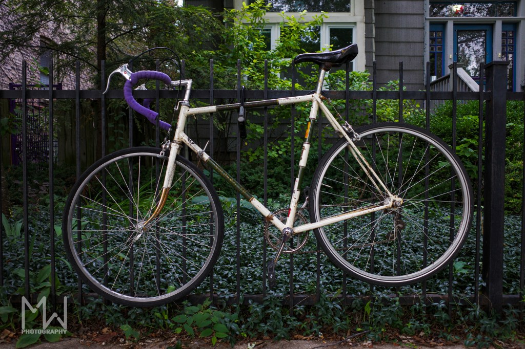 a bike chained to a iron fence with a house in the background